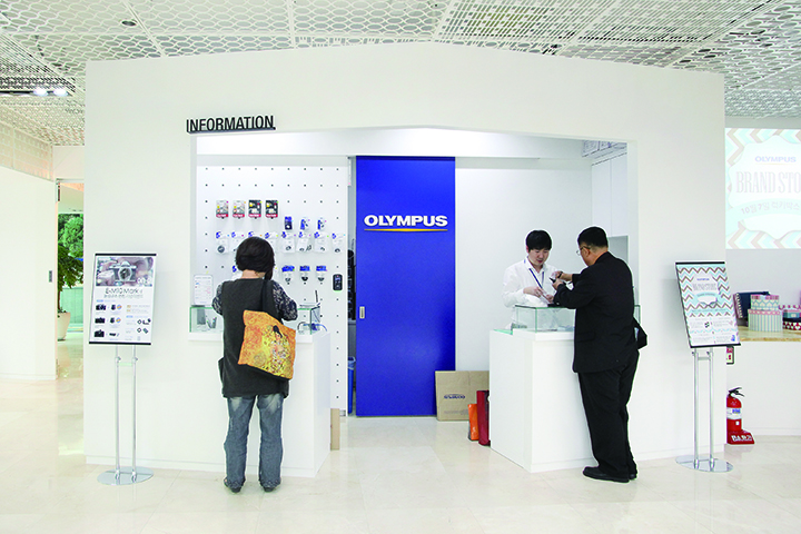 브랜드 매장에 관한 전반적인 정보를 제공하는 ‘인포데스크’다. 올림푸스 C.I가 부착된 파란색 벽이 포인트 역할을 한다. 

